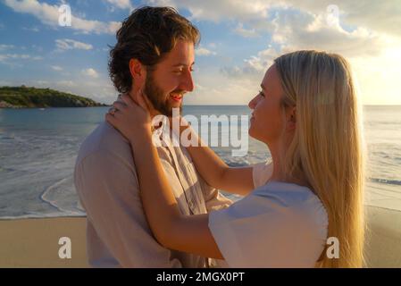 Couple récemment engagé appréciant une escapade romantique pendant l'heure d'or sur une plage de sable vide Banque D'Images