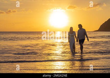Habillé jeune couple romantique marchant sur une plage tropicale de sable pendant le coucher de soleil sur l'océan Banque D'Images