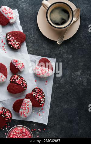 Des biscuits au velours rouge ou au brownie sur le cœur en forme de glaçage au chocolat avec des roses rouges sur fond noir. Idée de dessert pour la Saint-Valentin, les mères ou les femmes Banque D'Images
