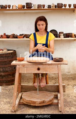 potier professionnel avec morceau d'argile dans les mains. femme travaille sur la roue de poterie à l'extérieur. photo verticale Banque D'Images