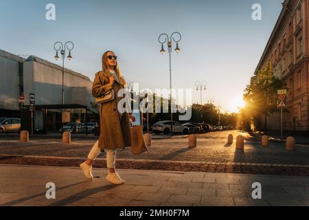 Une femme marche dans la rue de la ville le soir après avoir fait ses courses avec un sac en papier Banque D'Images