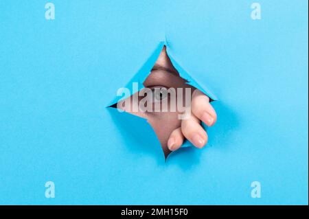 Une femme piquant hors de trou dans fond de papier bleu. Banque D'Images