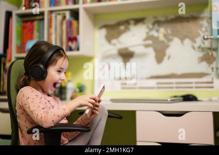 Une petite fille porte un casque pour regarder des dessins animés ou des vidéos d'enfant sur son téléphone. Banque D'Images