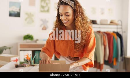Livraison, commande en ligne et femme à la mode sur ordinateur portable tout en travaillant dans une boutique. Jeune, heureux et Africain designer expédition de stock de vêtements dedans Banque D'Images