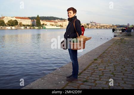 Femme revenant du marché agricole de Prague, debout près de la rivière et tenant un panier avec des microverts de pois Banque D'Images