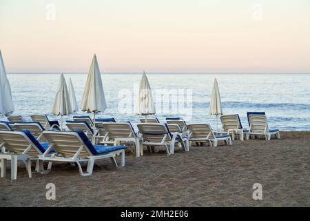 Vider les transats blancs et bleus sur la plage en bord de mer tôt le matin Banque D'Images