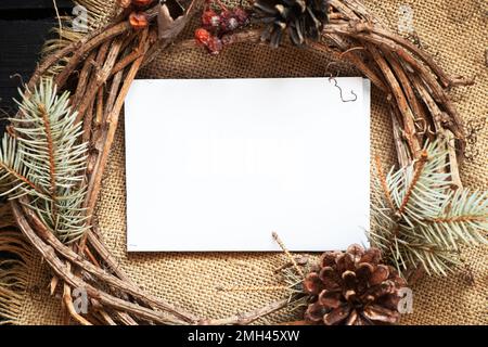 couronne de noël du nouvel an et au centre une carte en papier blanc pour le texte sur une ancienne table en bois, décor pour les vacances, une couronne d'une vigne sèche, un pla Banque D'Images