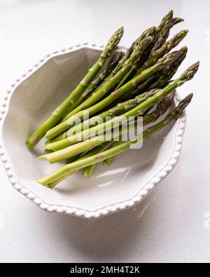 Asperges crues de sparagus, aspergus officinalis, dans un bol blanc sur fond blanc. Banque D'Images