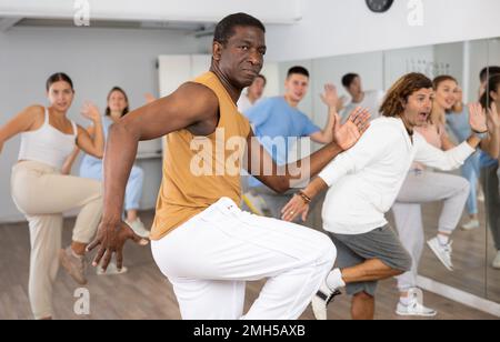 Homme afro-américain pratiquant des mouvements de danse actifs pendant la répétition avec un groupe en studio de danse. Banque D'Images