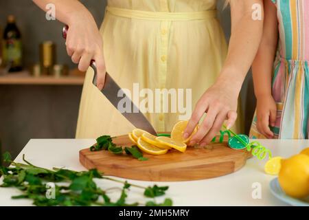 gros plan femme mains de couper le citron avec le couteau soigneusement. mère montre ses techniques de sécurité d'enfant dans la cuisine Banque D'Images
