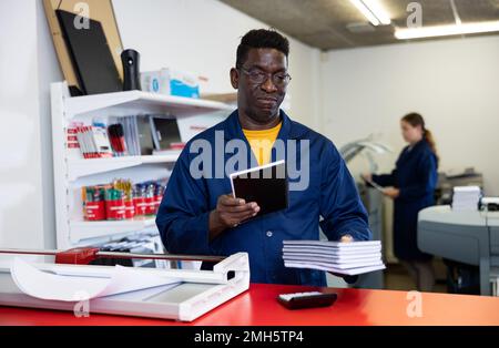 Portrait d'un sympathique employé de la maison d'impression avec pile de carnets dans ses mains Banque D'Images