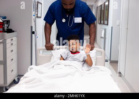 Afro-américain médecin poussant le jeune garçon patient dans le lit d'hôpital dans un couloir avec un espace de copie Banque D'Images