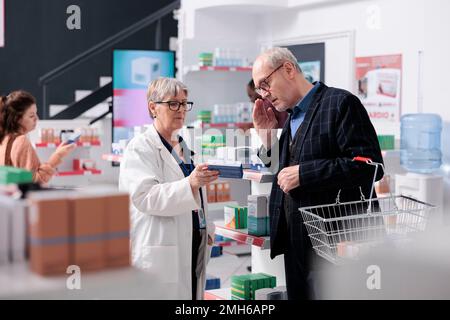 Un employé de pharmacie qui aide le client à traiter un médicament explique la notice de pilules cardiologiques pendant qu'il travaille en pharmacie. Un pharmacien qui donne de l'aide, un service de soins de santé Banque D'Images