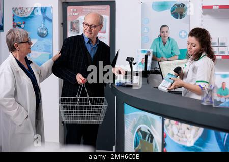 Homme senior mettant des boîtes de pilules sur le comptoir de pharmacie discutant de la brochure des produits avec le pharmacien avant de payer. Les employés de la pharmacie offrent de l'aide aux clients. Services de santé Banque D'Images