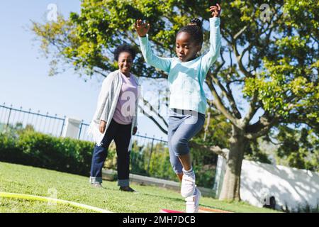 Bonne grand-mère afro-américaine et petite-fille utilisant la hula houle dans le jardin Banque D'Images