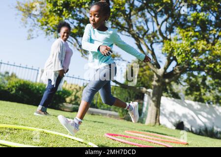 Bonne grand-mère afro-américaine et petite-fille utilisant la hula houle dans le jardin Banque D'Images