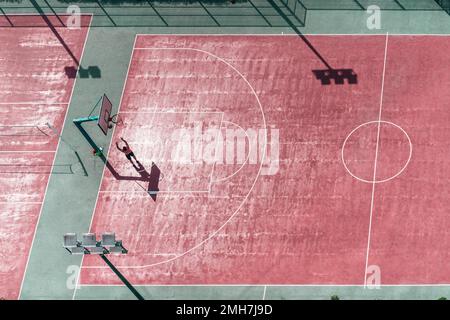 Vue sur un terrain de basket-ball coloré avec la silhouette d'un homme qui jette le ballon dans le panier ; vue depuis la hauteur au-dessus de la ba rouge et verte Banque D'Images