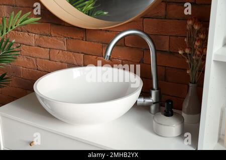 Lavabo en céramique, vase avec fleurs séchées et savon sur les tiroirs de la salle de bains Banque D'Images