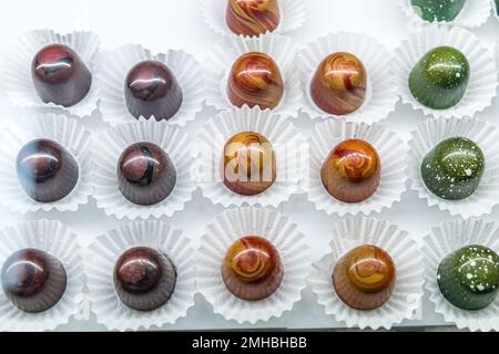 Un verre de confiserie au chocolat et de boulangerie présentant des truffes individuelles faites à la main dans une variété de couleurs et de saveurs avec des emballages en papier blanc Banque D'Images