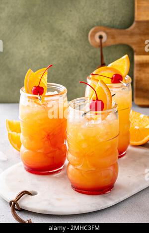 Punch au rhum dans des verres tiki avec des tranches d'orange et une cerise Banque D'Images