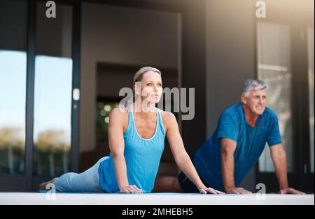 Commencez notre journée par une séance de yoga très nécessaire. Prise de vue en longueur d'un couple mature et heureux faisant des exercices de yoga à l'extérieur de leur maison. Banque D'Images