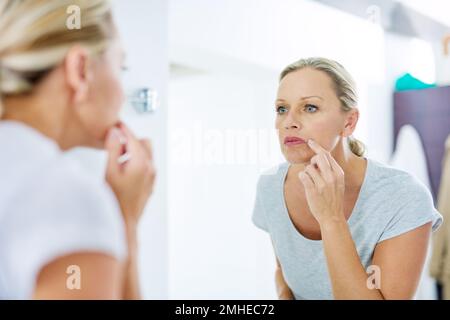 Il est temps de prendre soin de votre peau. une femme mûre inspectant sa peau devant le miroir de salle de bains. Banque D'Images