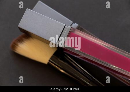 rouge à lèvres foncé et pinceau à poudre sur fond sombre, maquillage Banque D'Images