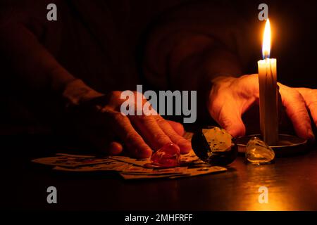 les mains se trouvent sur les cartes à jouer sur la table avec une bougie brûlante dans l'obscurité, la chance de dire sur les cartes, la magie Banque D'Images