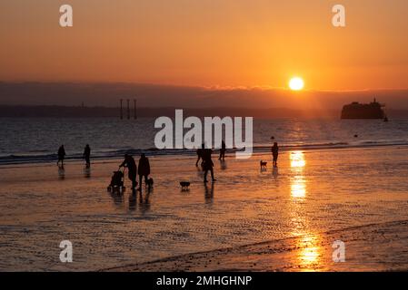 Vue sur le Solent au coucher du soleil sur le fort de Spitbank et l'île de Wight. Les gens marchent le long de la plage en profitant du coucher de soleil doré. Banque D'Images