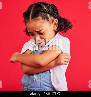 Enfant, bras croisés ou pleurs expression sur fond rouge isolé dans la dépression, la santé mentale ou l'épuisement professionnel. Contrarié, malheureux ou petite fille avec triste Banque D'Images