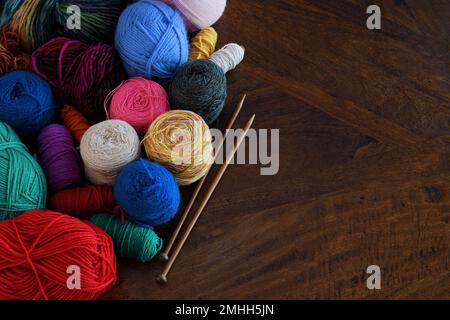 Un tas de montage de boules colorées de laine et d'aiguilles en bois à tricoter dans un éclairage doux avec un espace de copie à droite; capturé dans un studio Banque D'Images