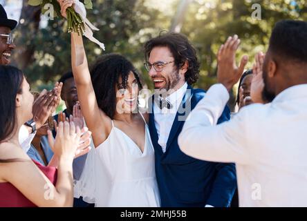 Bonne mariée et marié célébrer le mariage avec des applaudissements excités et joyeux dans la foule des invités. Amour interracial et bonheur de couple au mariage Banque D'Images