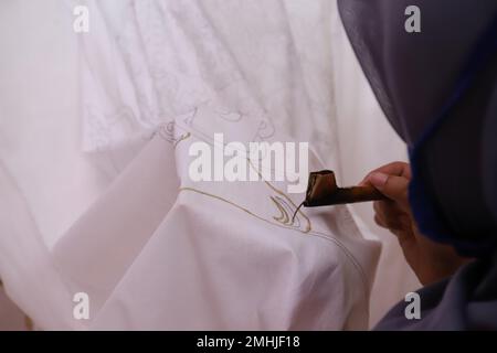 Une femme fait des croquis à la main avec des outils de cantage et de la cire chaude pour faire Batik traditionnel Banque D'Images