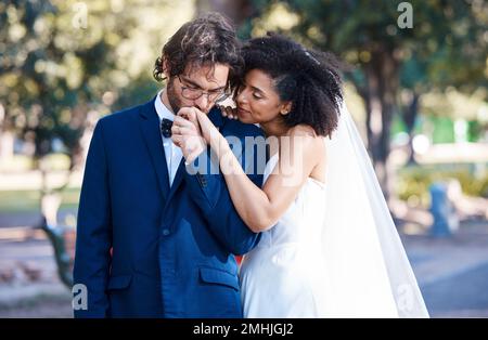 Mariage, couple et baiser tout en tenant les mains à l'extérieur à l'événement de célébration de mariage avec engagement. Homme et femme interraciaux avec confiance Banque D'Images