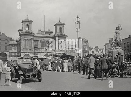 Une scène animée à la place du marché, Kingston upon Thames, dans le sud-ouest de Londres, Angleterre, Royaume-Uni vers 1910. La place du marché historique est en service depuis environ 1100s. Les étals vendent des produits de commerçants locaux. Le Royal Borough of Kingston upon Thames est situé à 10 miles (16 km) au sud-ouest du centre de Londres. Le bâtiment situé à l'arrière est l'ancien hôtel de ville, construit en 1838–40 par l'architecte Charles Henman l'aîné. À droite se trouve le Mémorial de Shrubsole, conçu par Francis John Williamson (1833–1920) en 1882 – une photographie vintage du début du 20th siècle. Banque D'Images