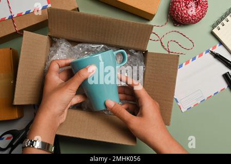 Vue en hauteur d'une femme mettant une tasse en céramique dans une boîte en carton, se préparant à emballer des cadeaux pour la période des fêtes Banque D'Images