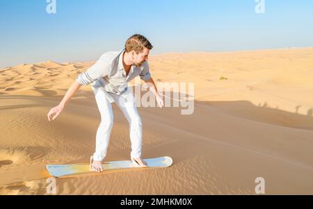 De jeunes hommes surfent sur les dunes de sable des Émirats arabes Unis de Dubaï, le désert de sable par une journée ensoleillée à Dubaï. Banque D'Images