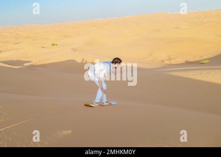 De jeunes hommes surfent sur les dunes de sable des Émirats arabes Unis de Dubaï, le désert de sable par une journée ensoleillée à Dubaï. Banque D'Images