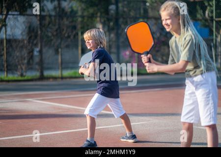Rire garçon et fille jouant au pickleball jeu, frapper pickleball jaune ...