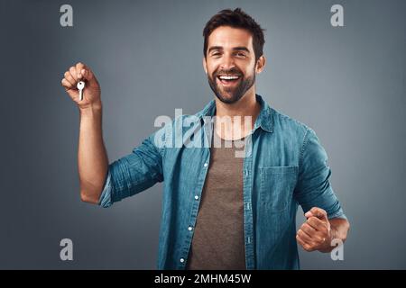 C'est super de l'appeler enfin le mien. Studio photo d'un jeune homme charmant tenant un ensemble de clés sur fond gris. Banque D'Images