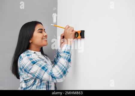 Une jeune femme sourit tout en utilisant le niveau d'esprit contre le mur faisant du bricolage à la maison Banque D'Images