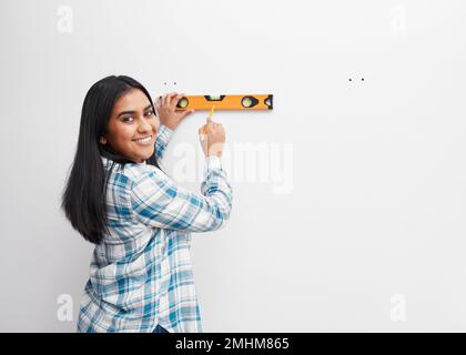 Une jeune femme sourit tout en utilisant le niveau d'esprit contre le mur faisant du bricolage à la maison Banque D'Images