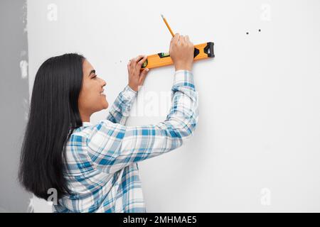 Une jeune femme sourit tout en utilisant le niveau d'esprit contre le mur faisant du bricolage à la maison Banque D'Images