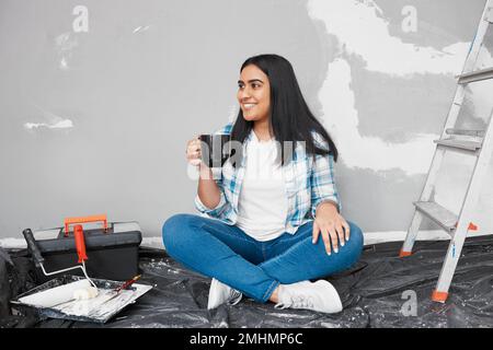 Une jeune femme indienne attrayante est assise sur le sol en prenant une pause café du bricolage Banque D'Images