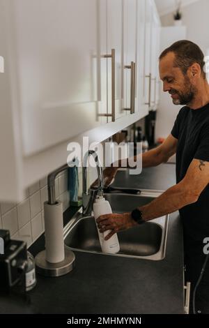 Homme remplissant la bouteille d'eau dans la cuisine Banque D'Images