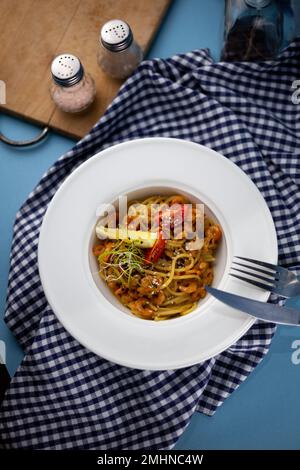 Spaghetti aux crevettes, citron et micro-vert. Déjeuner dans un plat blanc profond, gros plan. Pâtes avec fruits de mer, tomates et salade. Banque D'Images