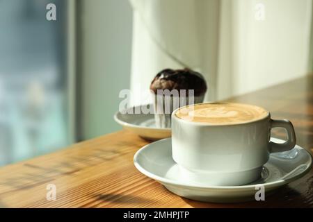 Tasse de café frais aromatique et cupcake à table dans le café Banque D'Images