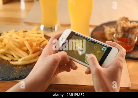 Femme jouant au jeu en utilisant un smartphone à la table avec de savoureux en-cas, gros plan Banque D'Images