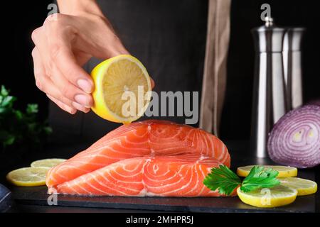 Femme pressant le citron sur le saumon frais cru à la table, gros plan. Délicatesse du poisson Banque D'Images