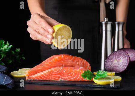 Femme pressant le citron sur le saumon frais cru à la table, gros plan. Délicatesse du poisson Banque D'Images